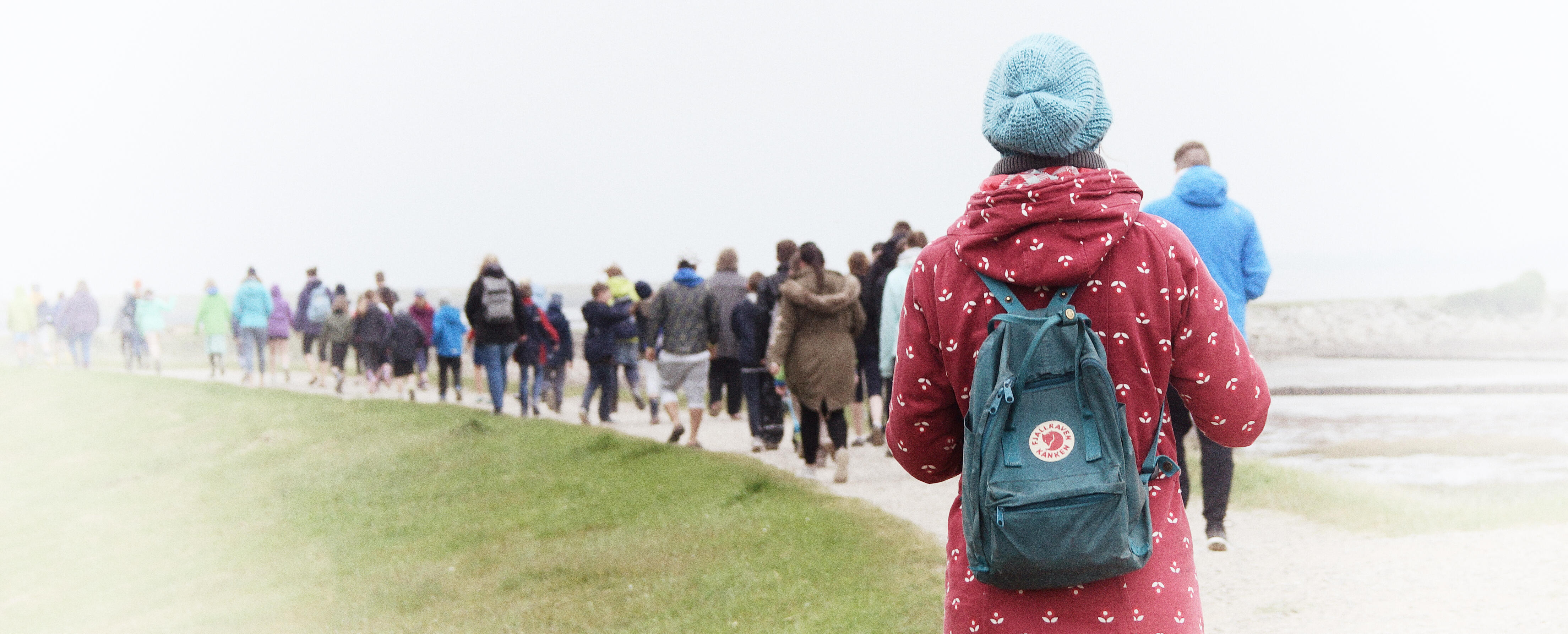 Foto: Schulkinder gehen auf einem Deich. Man sieht sie von hinten.