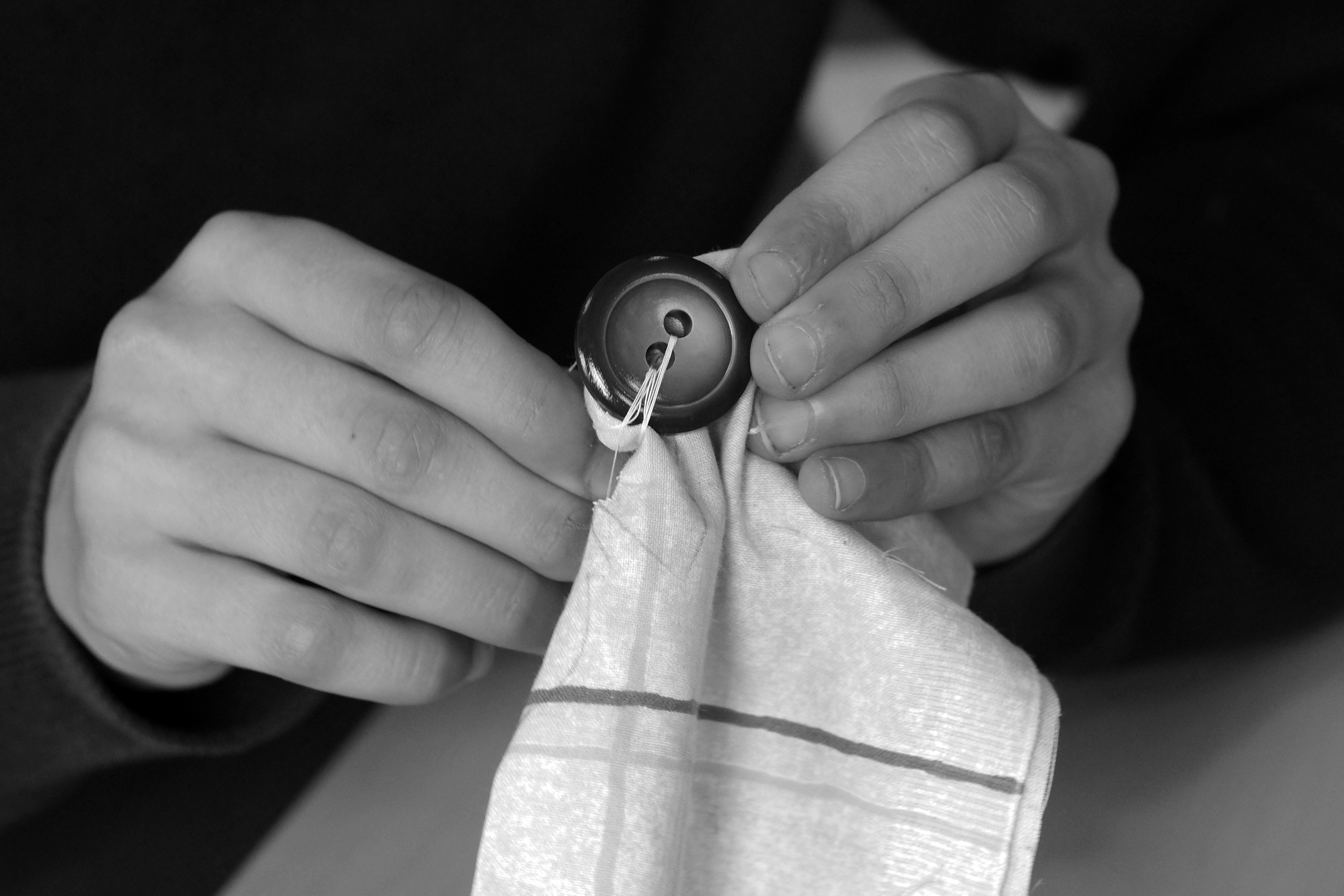 Foto: Zwei Hände, die einen Knopf an ein Tuch nähen.