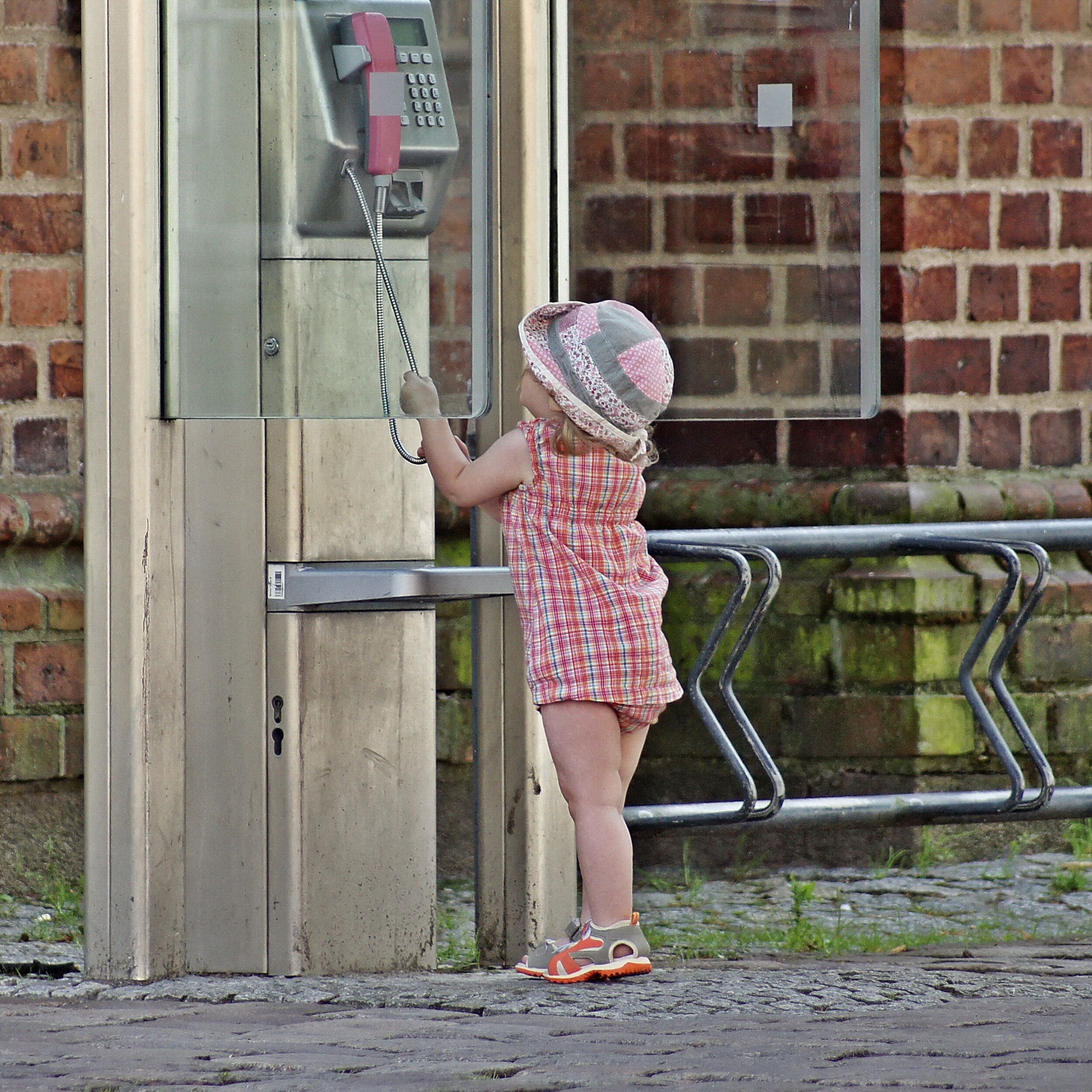 Ein Kind zieht an der Schnur eines öffentlichen Telefons.